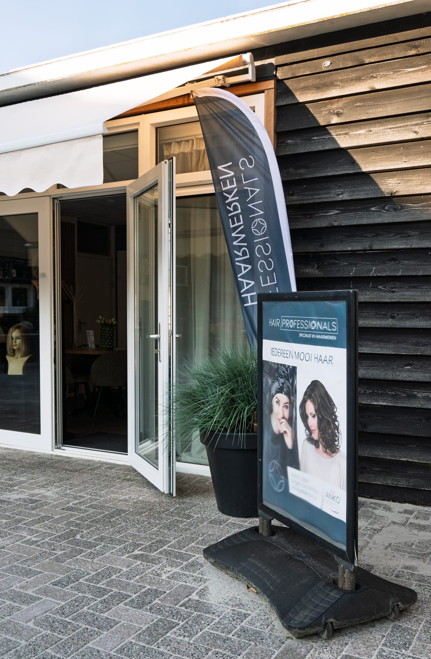 De entree van Hair Professionals met openstaande deuren en planten aan weerszijden.